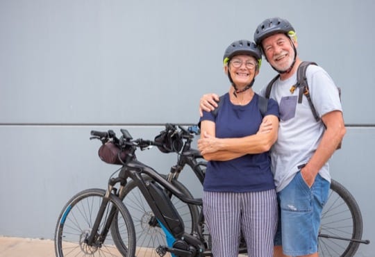 Happy and relaxed senior caucasian couple with helmet enjoying sport activity with electric bicycles in outdoors – sustainable mobility concept
